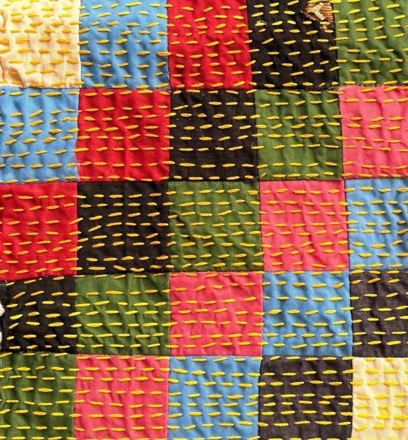 Close-up of brightly coloured cloth squares, each crossed by short rows of yellow running stitch.