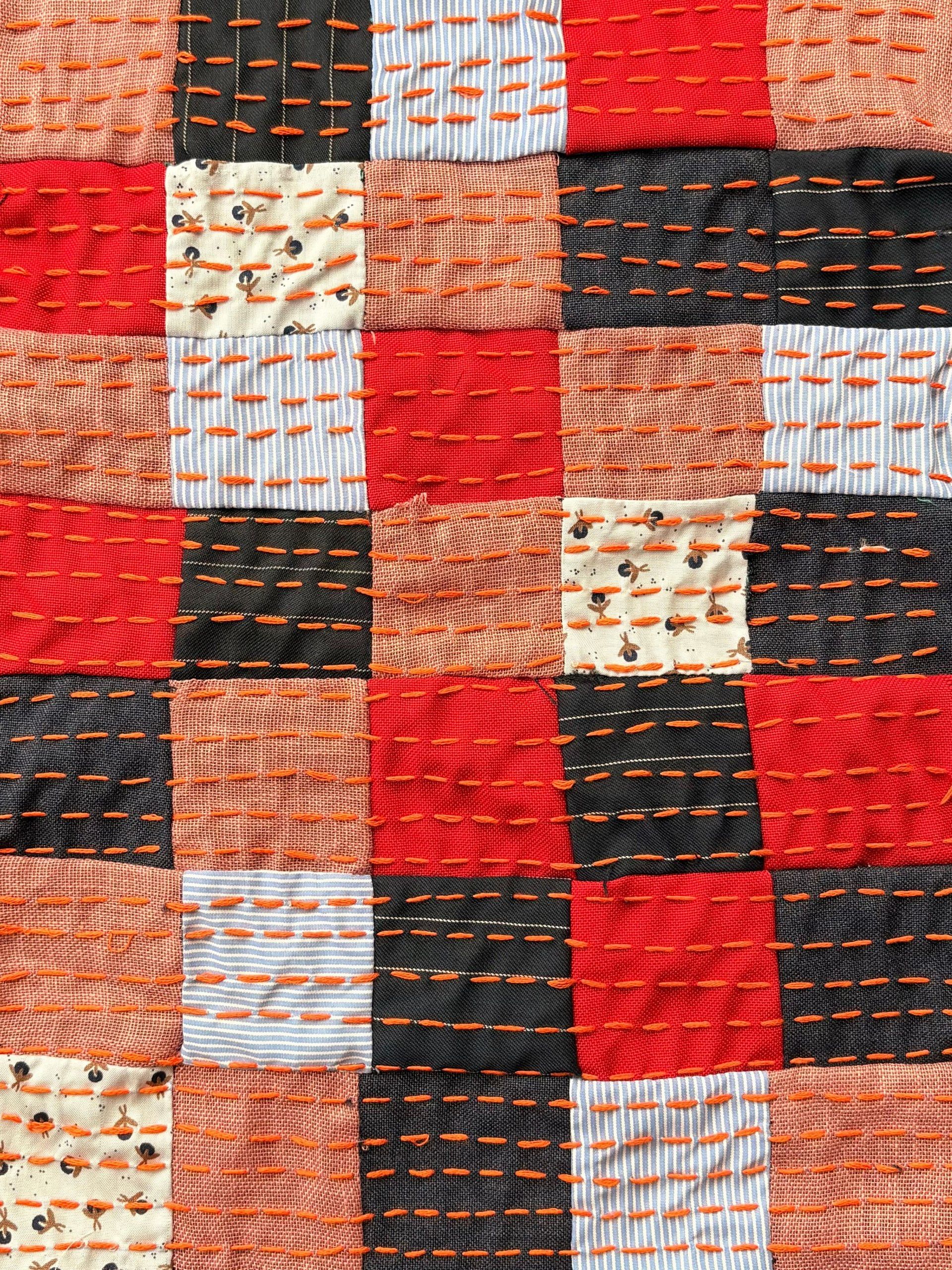 Close-up of red, black, orange and printed squares joined by rows of orange running stitch.