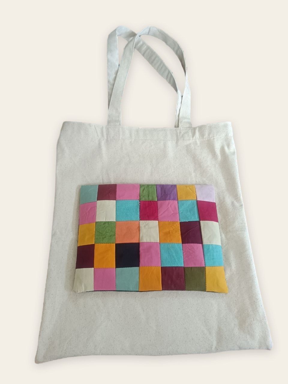A plain cotton tote bag with a panel of coloured squares on its front.