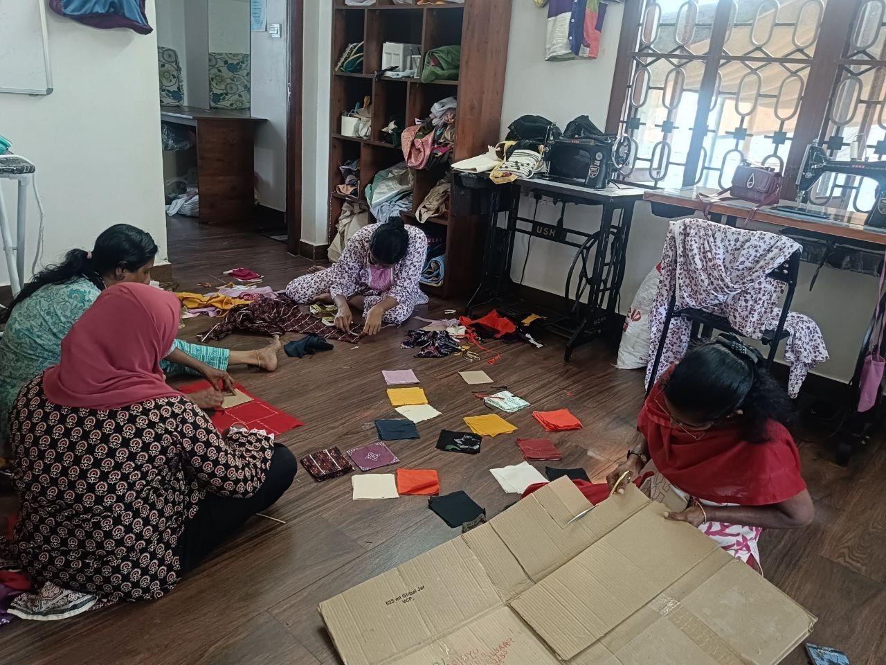 Makers sit on a workshop floor with squares of cloth spread out around them.