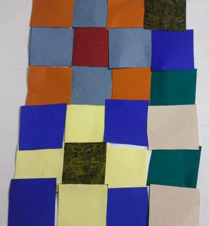 Squares of plain and printed cloth in blue, orange, yellow and green, overlapping in rows on a white background.