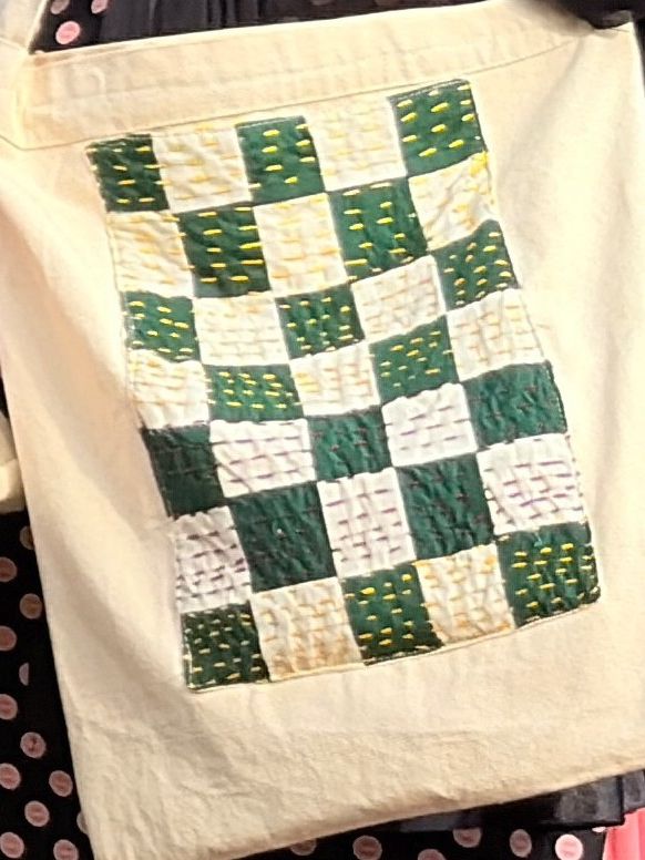 A cotton tote bag with a green and cream chess panel of stitched squares on its front.