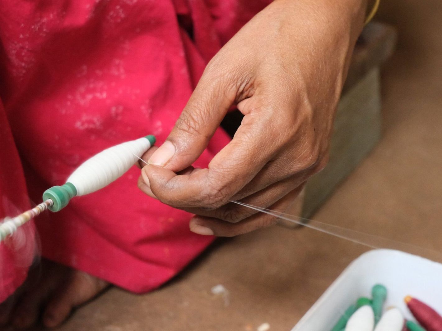 A weaver's hand guiding cotton thread onto a bobbin.