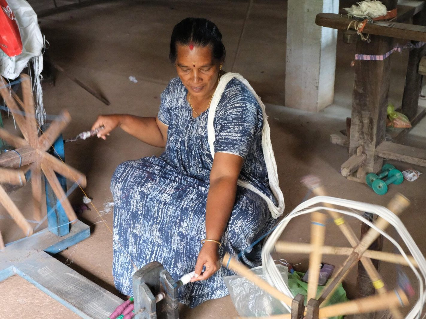 A weaver at the charkha, winding yarn onto bobbins.